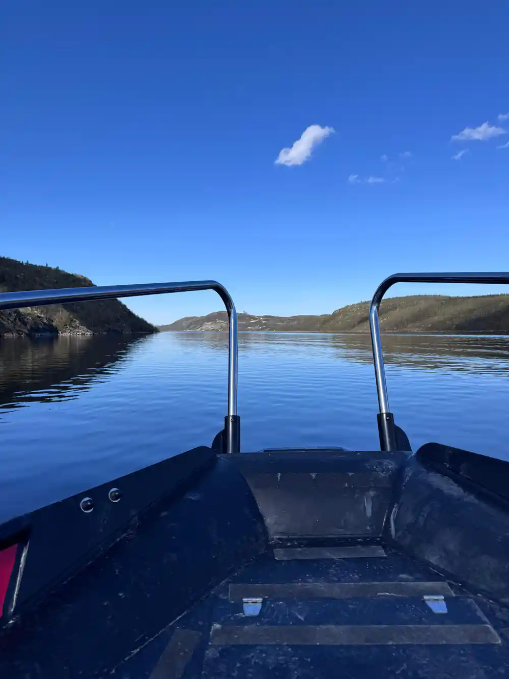 Calm blue fjord and low hills seen over the bow