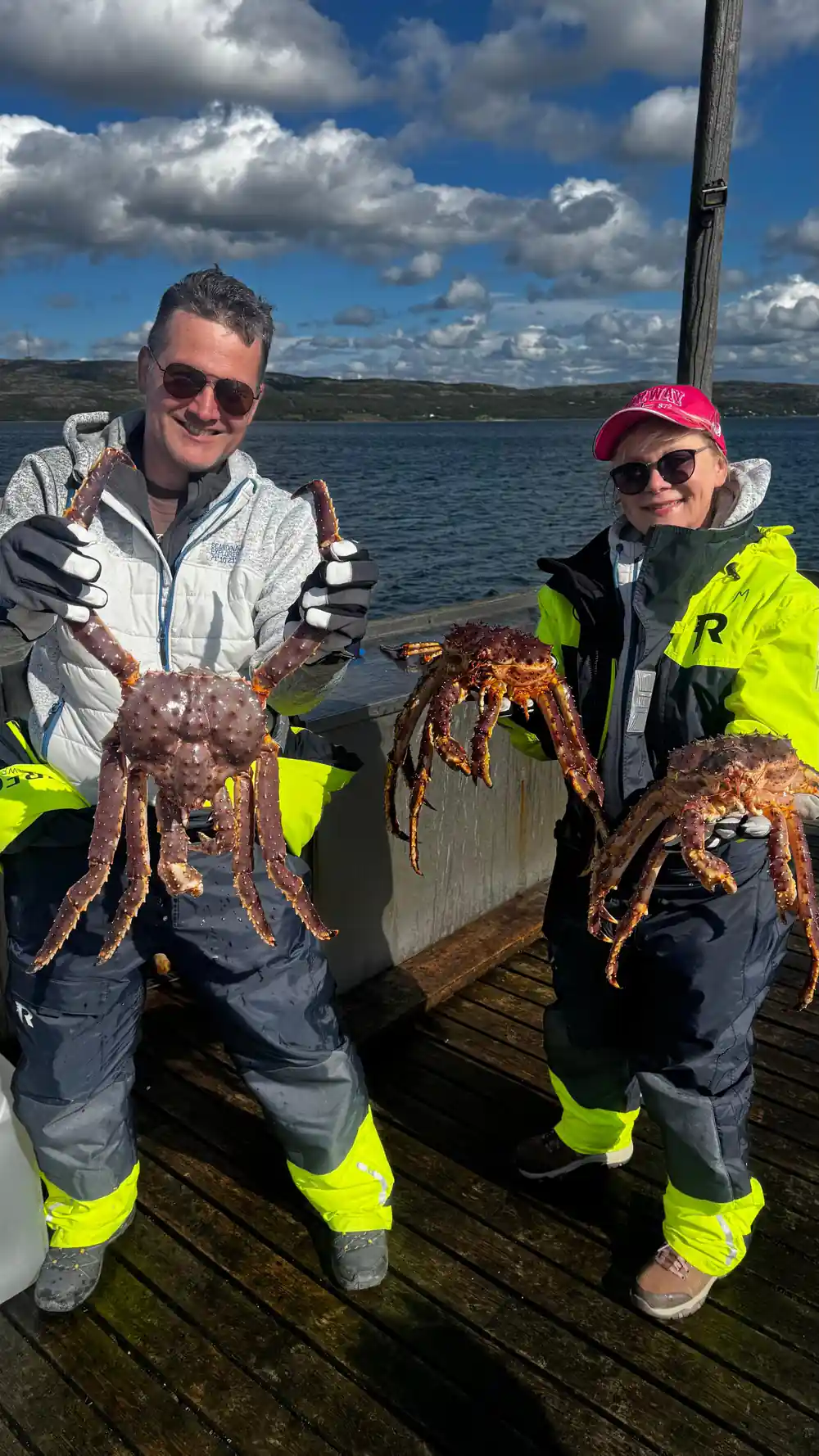 A couple in flotation suits each holding a king crab